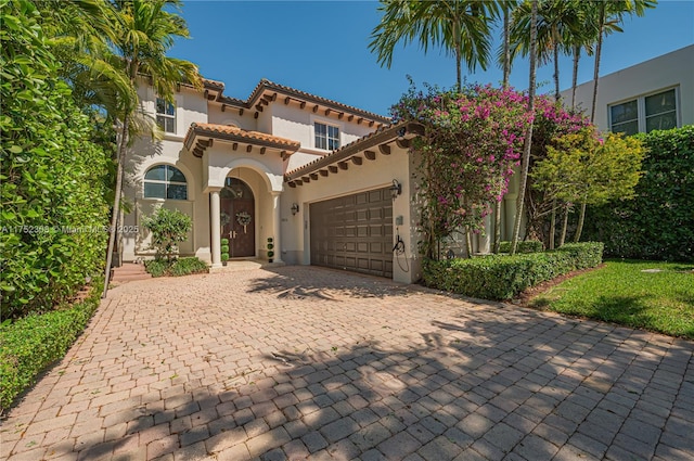 mediterranean / spanish house featuring a tiled roof, stucco siding, an attached garage, and decorative driveway