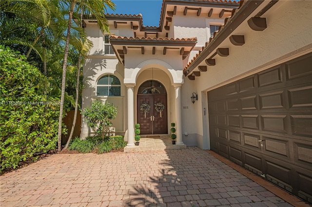 entrance to property with stucco siding, a tile roof, decorative driveway, french doors, and a garage