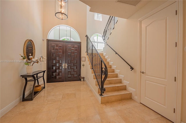 tiled entrance foyer featuring a high ceiling, stairway, baseboards, and visible vents