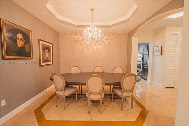 dining space featuring an accent wall, a raised ceiling, baseboards, and ornamental molding