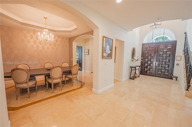 foyer featuring an accent wall, baseboards, a chandelier, arched walkways, and a raised ceiling