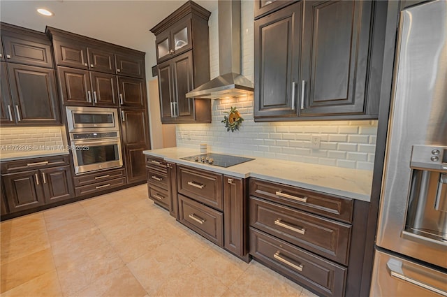 kitchen with tasteful backsplash, stainless steel appliances, wall chimney range hood, light stone countertops, and dark brown cabinets