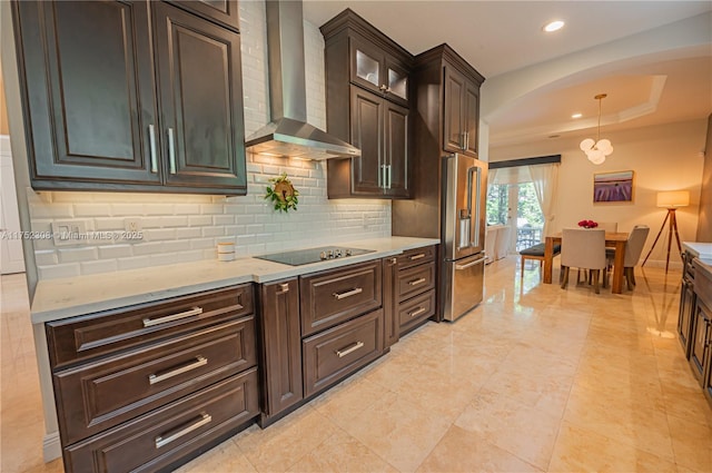 kitchen featuring black electric stovetop, wall chimney range hood, a tray ceiling, high end refrigerator, and arched walkways