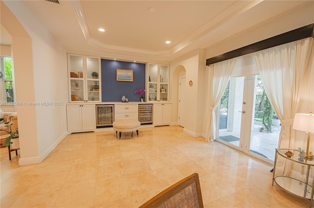 living area with beverage cooler, a healthy amount of sunlight, built in shelves, and a raised ceiling