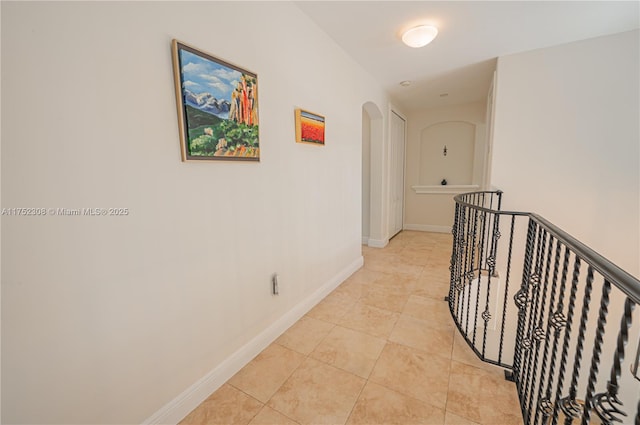 hall with light tile patterned flooring, baseboards, arched walkways, and an upstairs landing