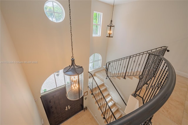 stairway featuring tile patterned flooring, a high ceiling, and baseboards