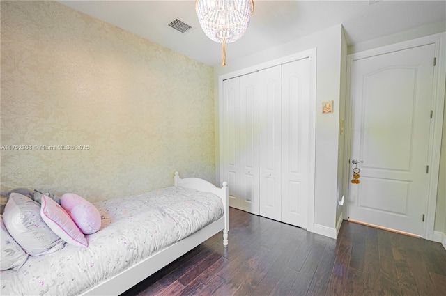 bedroom with an inviting chandelier, wood finished floors, visible vents, and a closet