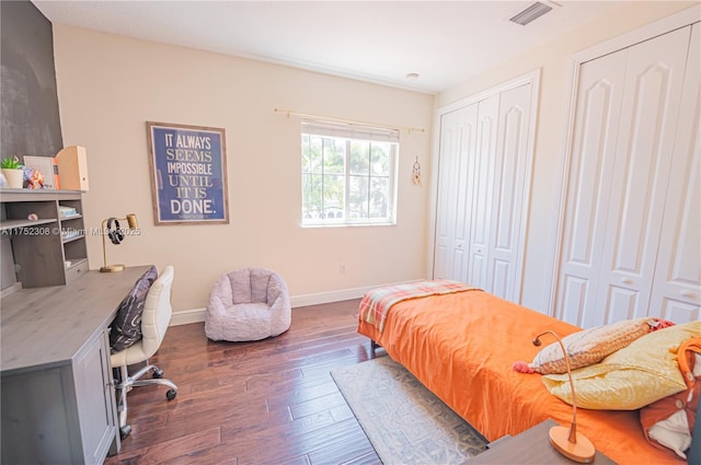 bedroom with dark wood-style floors, visible vents, baseboards, and multiple closets