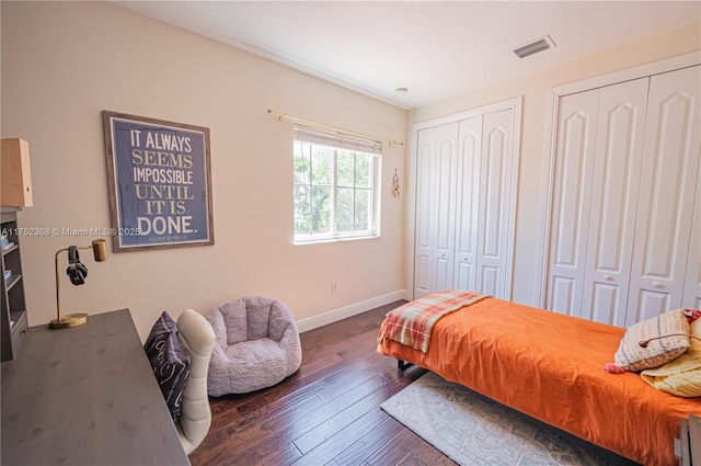 bedroom with wood-type flooring, baseboards, visible vents, and two closets