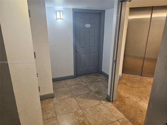 hallway featuring tile patterned flooring, elevator, and baseboards