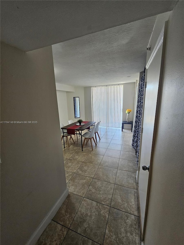 hall featuring tile patterned flooring, a textured ceiling, and baseboards