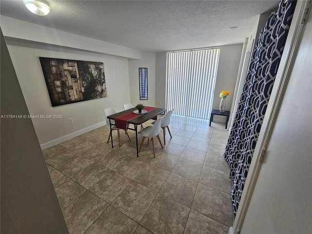 dining space with dark tile patterned flooring, baseboards, and a textured ceiling