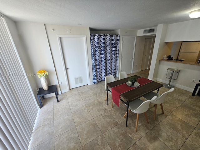 dining area featuring light tile patterned floors, visible vents, baseboards, and a textured ceiling