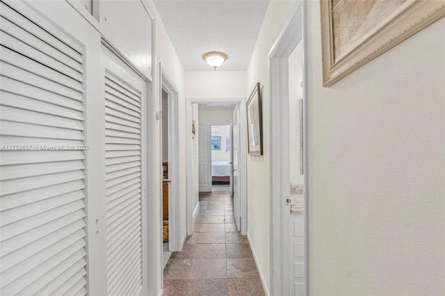 hall featuring baseboards and stone tile flooring