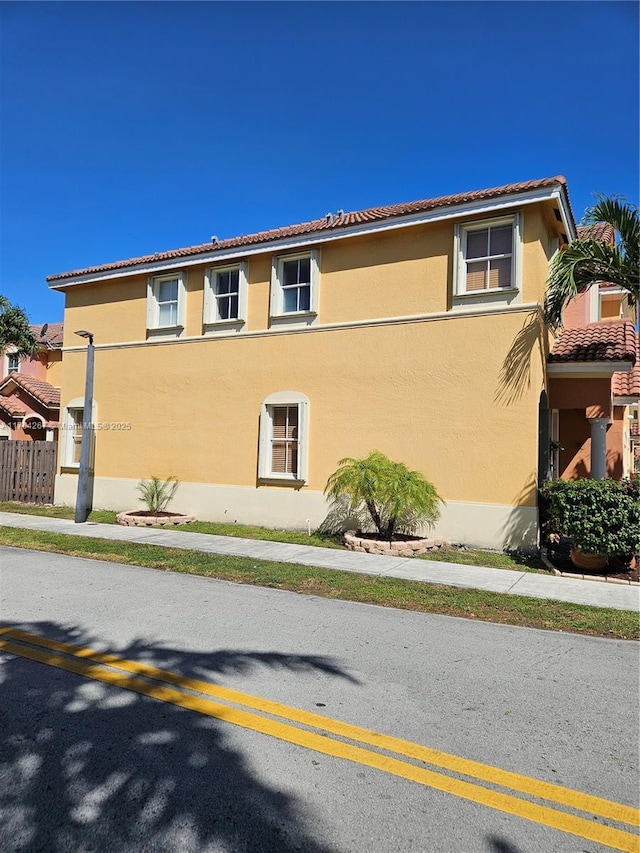 view of property exterior with stucco siding, a tiled roof, and fence