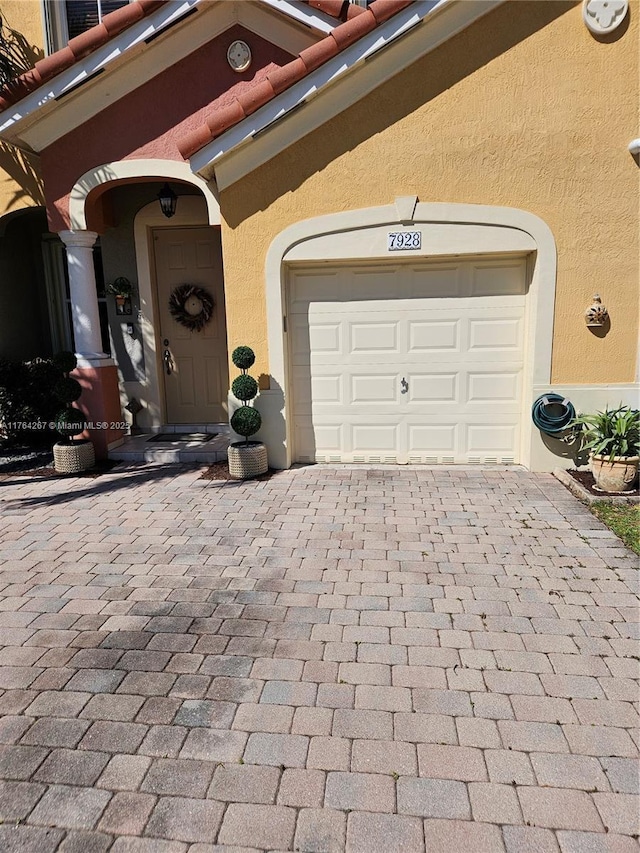 view of exterior entry with stucco siding, a tiled roof, an attached garage, and decorative driveway