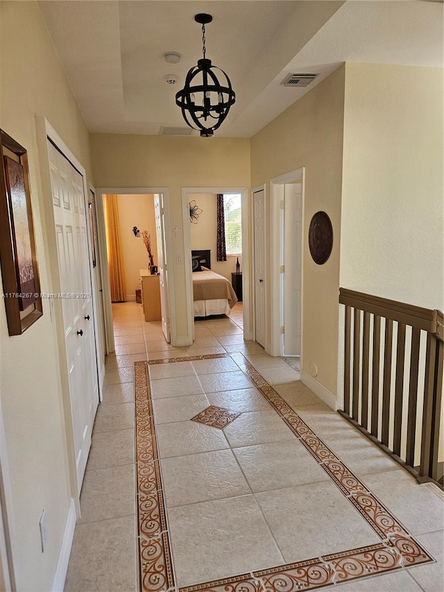 corridor featuring visible vents, an inviting chandelier, a raised ceiling, and baseboards