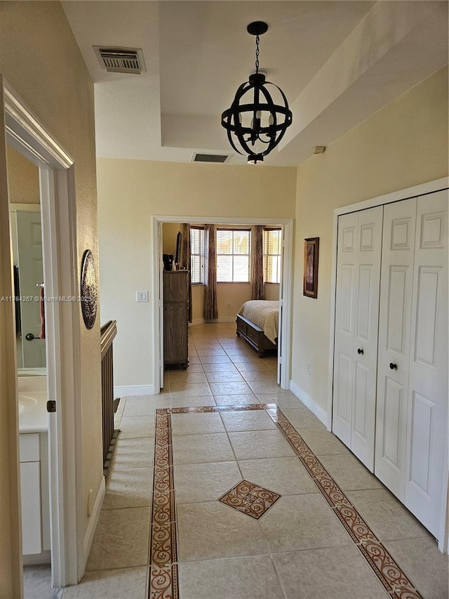 corridor with a notable chandelier, visible vents, a raised ceiling, and baseboards