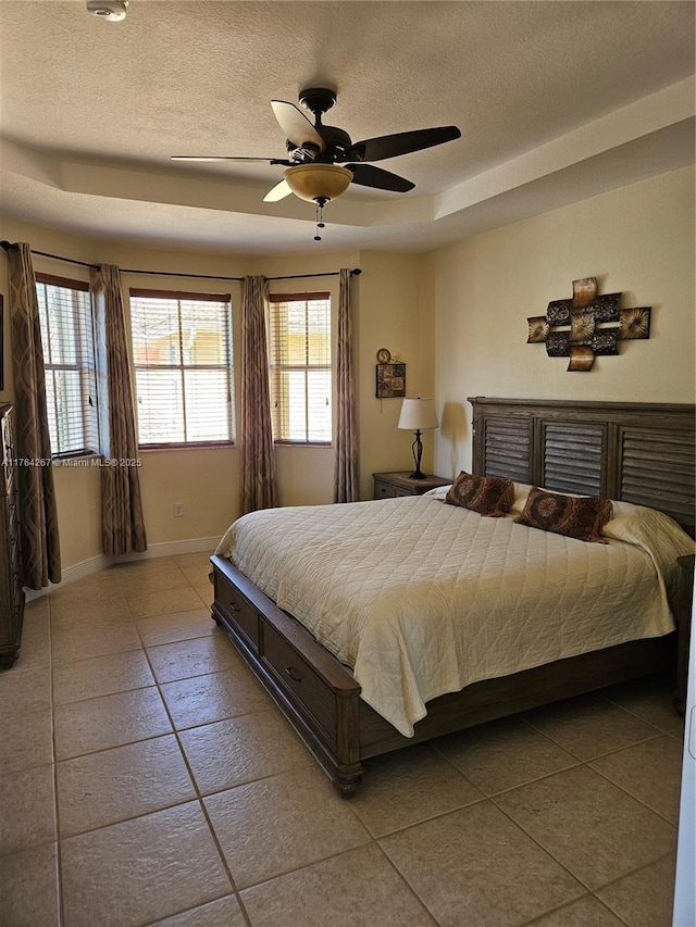 bedroom featuring a tray ceiling, a ceiling fan, baseboards, and a textured ceiling