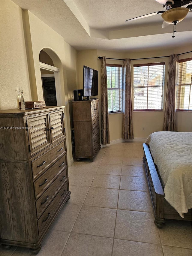 bedroom featuring a raised ceiling, a textured ceiling, arched walkways, light tile patterned floors, and baseboards