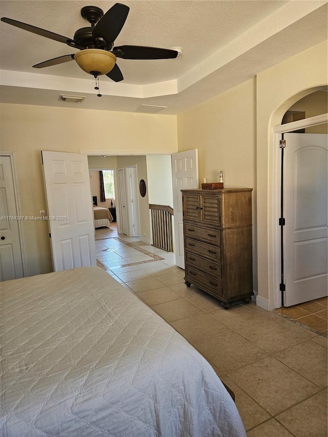 bedroom with visible vents, a tray ceiling, a textured ceiling, arched walkways, and baseboards