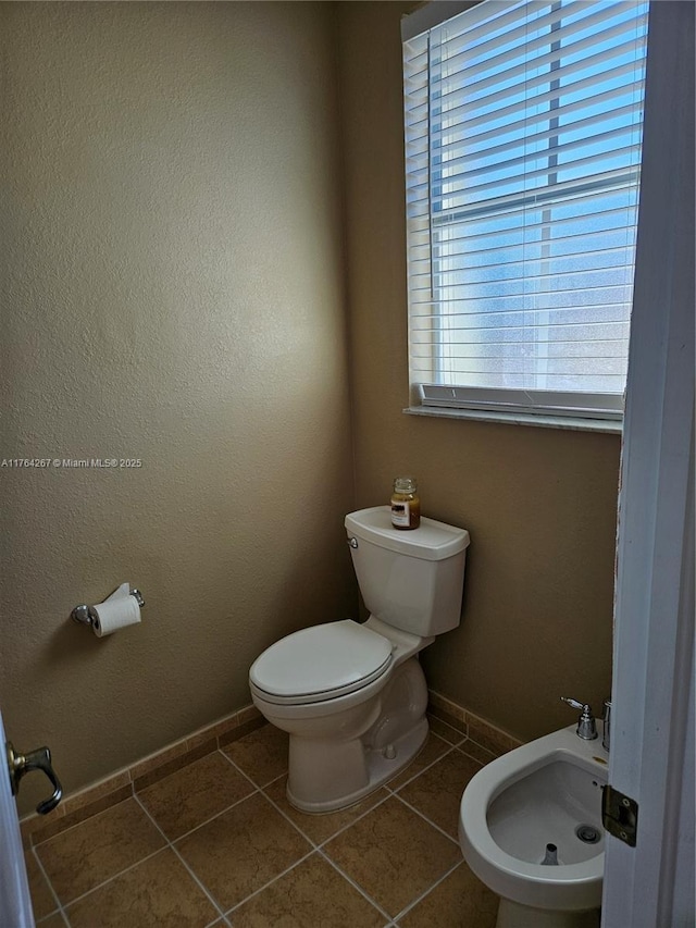 half bathroom with tile patterned flooring, toilet, a bidet, and baseboards