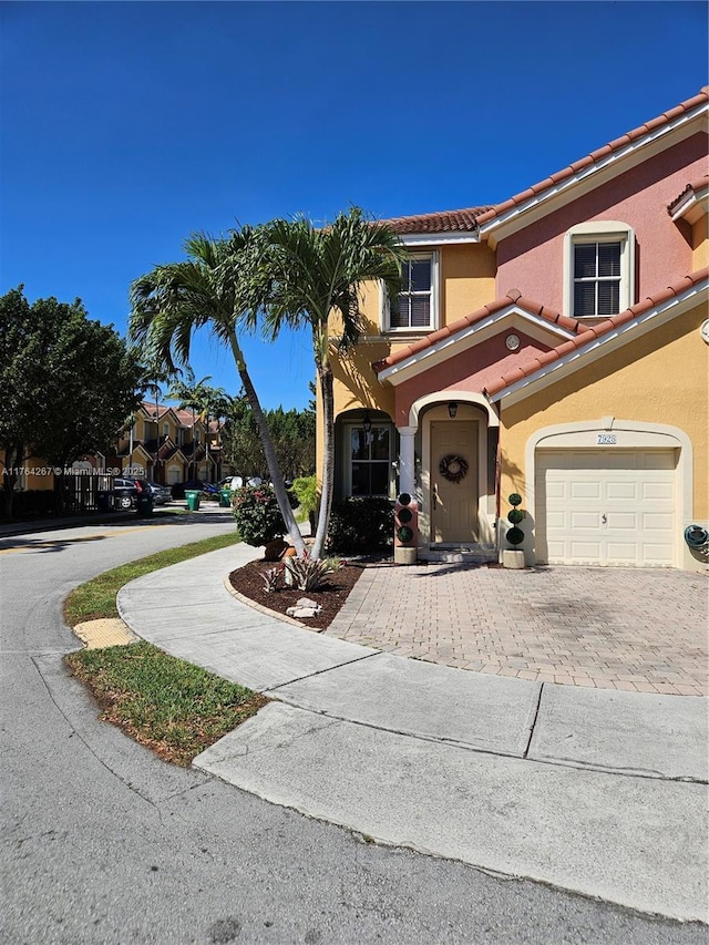 mediterranean / spanish-style home featuring stucco siding, a tiled roof, decorative driveway, and a garage