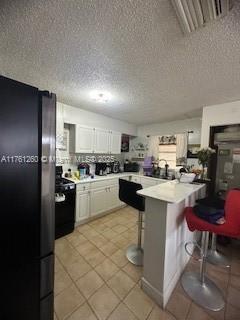 kitchen with light tile patterned floors, visible vents, a peninsula, black appliances, and a kitchen breakfast bar