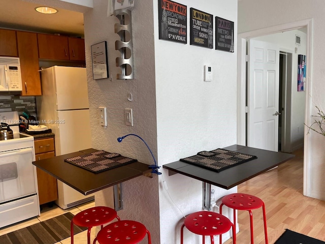 kitchen featuring white appliances, brown cabinetry, a textured wall, light wood-type flooring, and backsplash