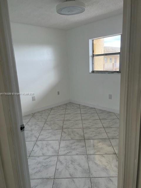 unfurnished room featuring light tile patterned floors, baseboards, and a textured ceiling