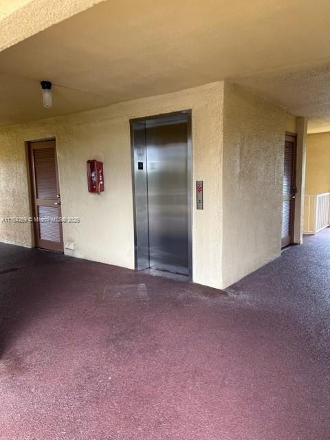 exterior space featuring elevator, dark carpet, and a textured wall