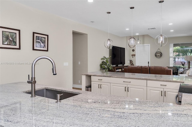 kitchen featuring light stone counters, visible vents, white cabinets, and a sink