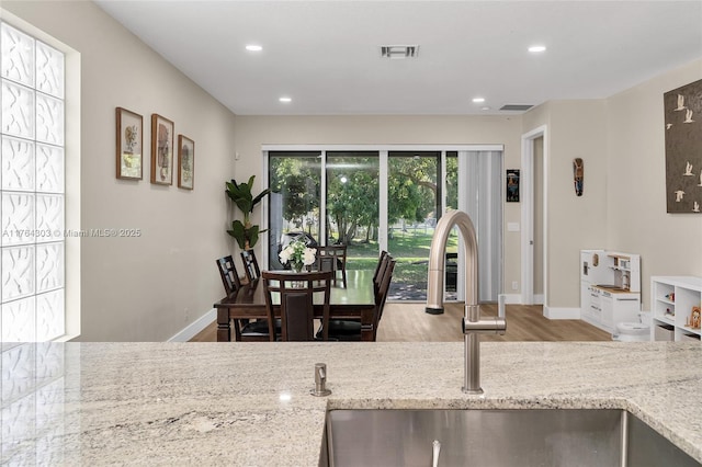 kitchen with visible vents, light stone countertops, wood finished floors, and a sink