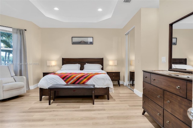 bedroom with baseboards, a raised ceiling, and light wood-style floors