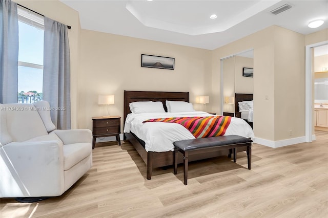 bedroom featuring visible vents, baseboards, a raised ceiling, and light wood-style floors