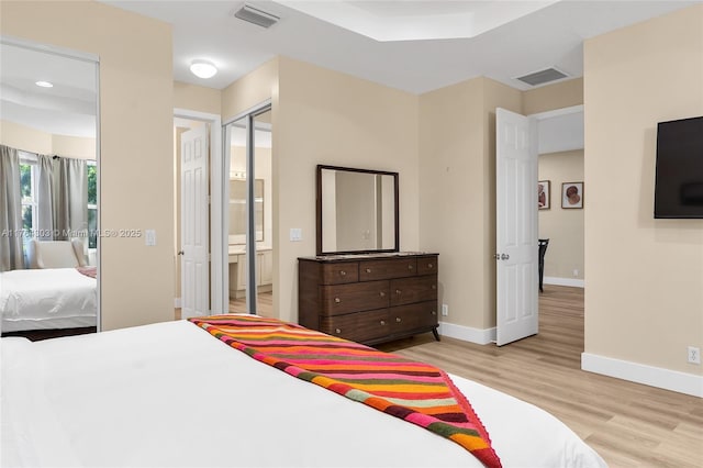 bedroom featuring visible vents, ensuite bath, light wood-type flooring, and baseboards