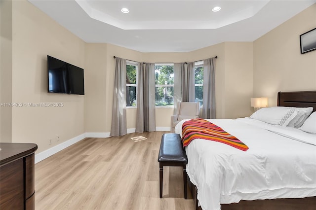 bedroom featuring a raised ceiling, recessed lighting, light wood-style floors, and baseboards