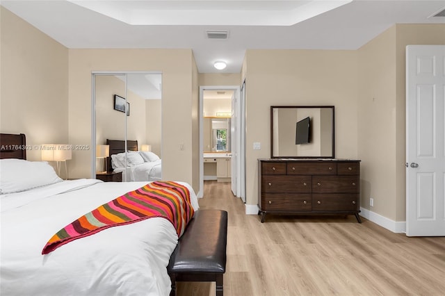 bedroom featuring a tray ceiling, visible vents, baseboards, and light wood finished floors