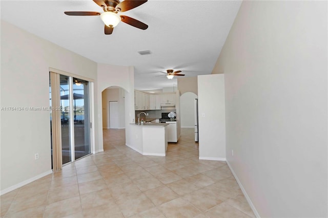 unfurnished living room featuring a ceiling fan, visible vents, baseboards, arched walkways, and a sink