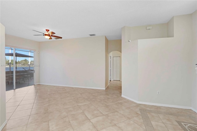 unfurnished room with visible vents, a ceiling fan, arched walkways, light tile patterned flooring, and baseboards