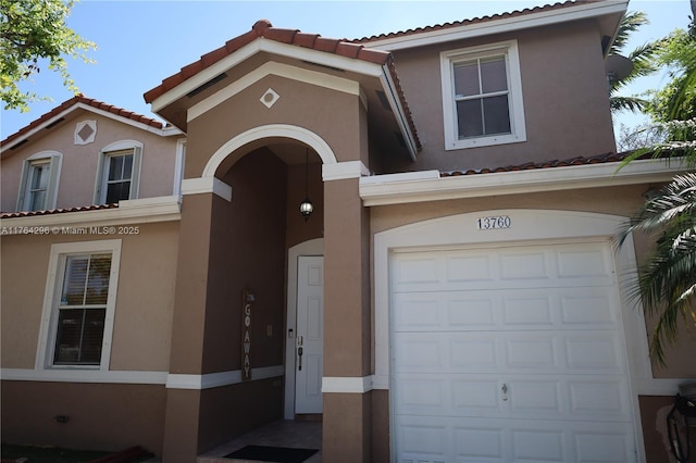 mediterranean / spanish home featuring stucco siding, an attached garage, and a tile roof