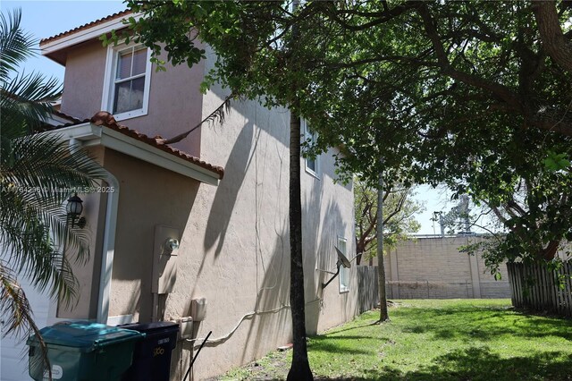 view of home's exterior featuring stucco siding, a tile roof, a yard, and fence