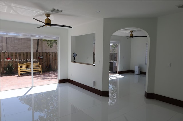 tiled empty room with visible vents, arched walkways, baseboards, and a ceiling fan