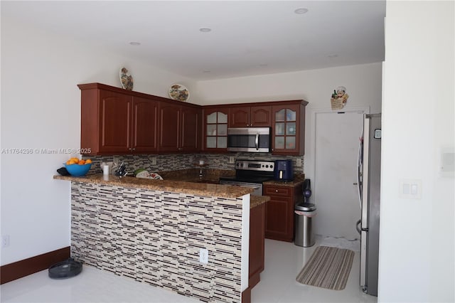 kitchen featuring glass insert cabinets, light tile patterned floors, decorative backsplash, appliances with stainless steel finishes, and a peninsula