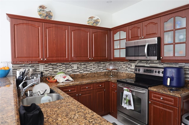 kitchen with tasteful backsplash, glass insert cabinets, stone countertops, stainless steel appliances, and a sink