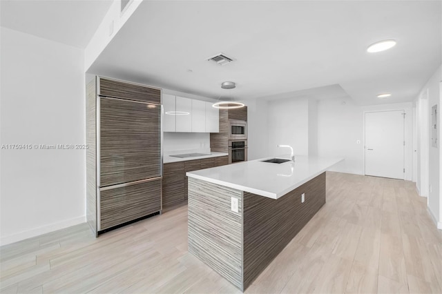 kitchen featuring modern cabinets, a sink, white cabinets, light countertops, and built in appliances