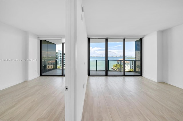 unfurnished room with floor to ceiling windows, light wood-style flooring, and baseboards