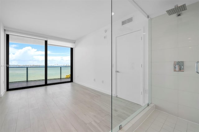 bathroom featuring visible vents, baseboards, expansive windows, a tile shower, and wood finished floors