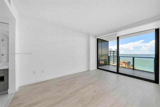 unfurnished room featuring a wall of windows, baseboards, light wood-style flooring, and a water view