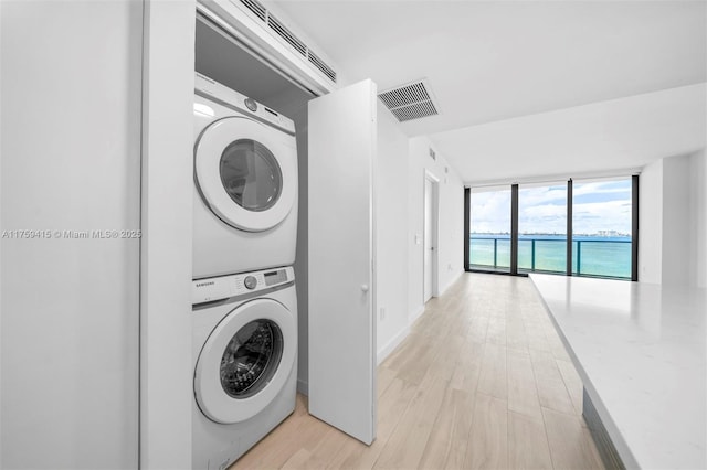 laundry room featuring light wood-type flooring, stacked washer / dryer, laundry area, and visible vents